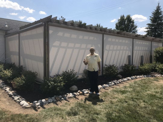Image of pergola structure with light grey motorized shades and a man standing in front with his thumb raised.